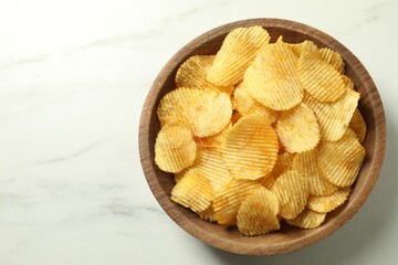 Tasty potato chips in bowl on white marble table, top view. Space for text
