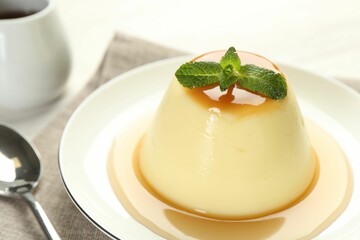Delicious pudding with caramel sauce and mint served on white table, closeup