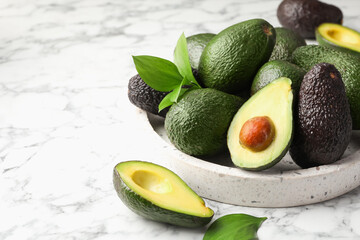 Whole and cut avocados on white marble table, closeup. Space for text