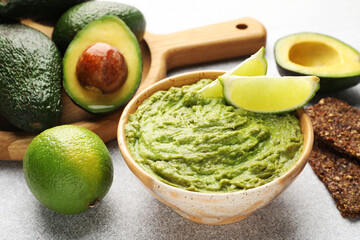 Tasty avocado dip, lime and crispbreads on light grey table, closeup