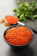 Tasty red caviar in bowl, spoon and parsley on grey table, closeup