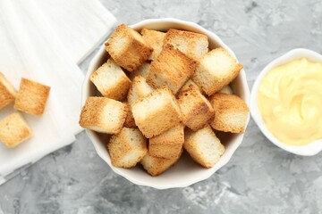 Tasty crispy croutons and sauce on grey textured table, flat lay