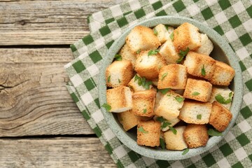 Tasty crispy croutons with cut parsley in bowl on wooden table, top view. Space for text