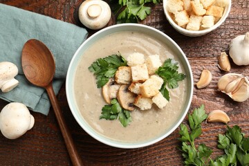 Delicious mushroom cream soup with croutons, parsley, ingredients and spoon on wooden table, flat lay
