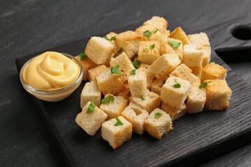 Tasty crispy croutons with cut parsley and sauce on dark textured table, closeup