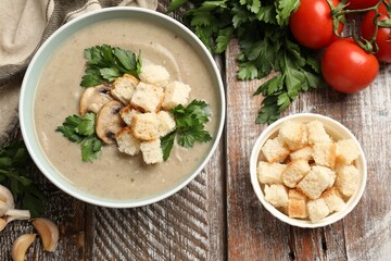 Delicious mushroom cream soup with croutons and ingredients on wooden table, flat lay