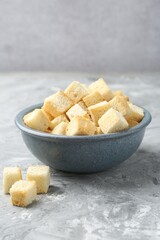 Tasty crispy croutons in bowl on grey textured table, closeup