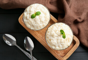 Delicious rice pudding with mint and spoons on black wooden table, flat lay