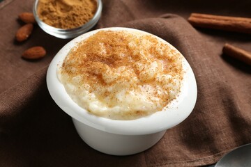 Delicious rice pudding with cinnamon in bowl and almonds on table, closeup