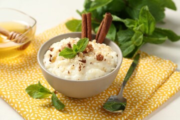 Delicious rice pudding with walnuts, cinnamon, mint and honey on white table, closeup