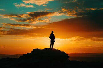 Silhouette of a man standing on a rock, watching a vibrant sunset over a mountain range.