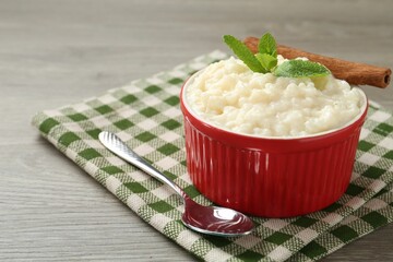 Delicious rice pudding with cinnamon, mint and spoon on wooden table, closeup. Space for text