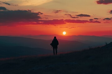 Fototapeta premium Silhouette of a person standing on a hilltop, witnessing a breathtaking sunset over a vast mountainous landscape.