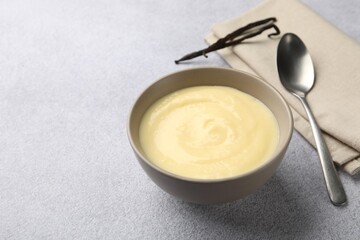 Tasty vanilla pudding in bowl, pods and spoon on light grey table, closeup. Space for text
