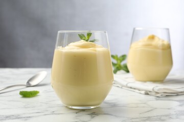 Tasty vanilla pudding with mint on white marble table