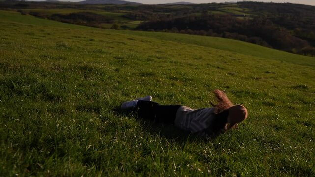Girl rolling down a hill in a field at sunset