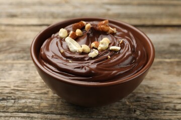Delicious chocolate pudding with nuts in bowl on wooden table, closeup