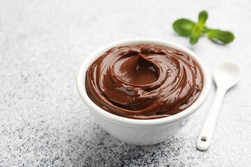 Delicious chocolate pudding in bowl and spoon on light grey textured table, closeup. Space for text
