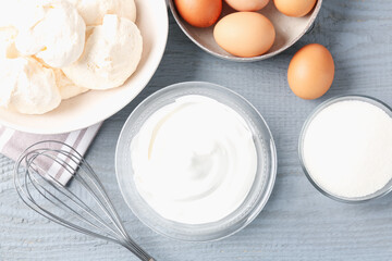 Delicious homemade meringue cookies, ingredients and whisk on gray wooden table, flat lay