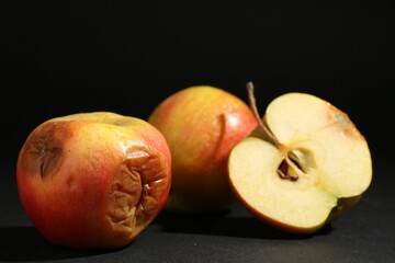 Cut and whole rotten apples on black background, closeup