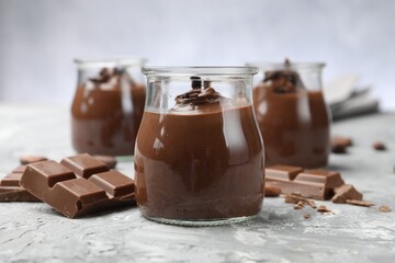 Tasty pudding in glass jars and pieces of chocolate on light grey table, closeup