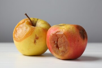 Rotten apples on white wooden table against grey background, closeup