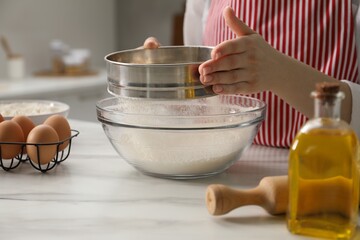 Making khinkali. Woman sieving flour into bowl at table in kitchen, closeup