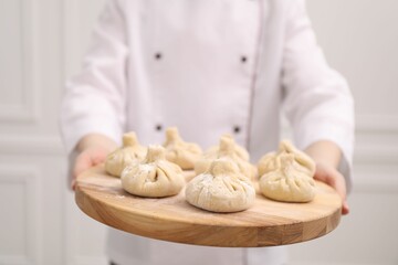 Chef holding board with uncooked khinkali indoors, closeup