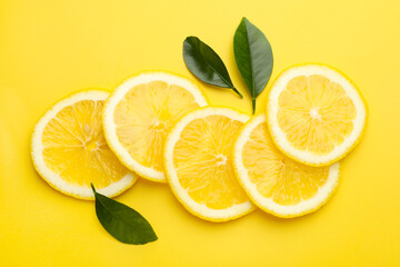 Slices of fresh lemons and green leaves on yellow background, flat lay