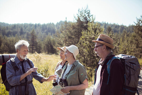 Group of senior hikers navigating forest trail with map near river