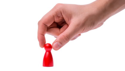 A hand holding a small red wooden pawn, symbolizing choice and decision-making.  The pawn is being picked up, highlighting the power of the individual's choice