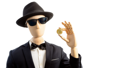 a wooden figure, dressed in a black suit, hat, and sunglasses, is holding a gold coin in its hand
