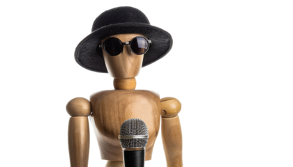 A wooden mannequin with a hat and sunglasses holding a microphone, ready to speak. This photo evokes a sense of performance and mystery.