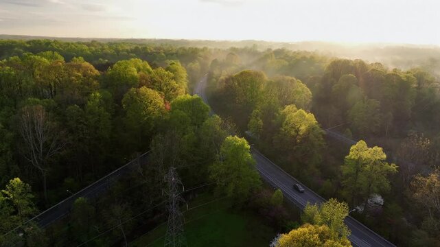 Cars driving on suburb interstate road in American. during golden sunrise. Mystic fog fling between green and yellow colored trees. Aerial establishing wide shot scene in USA.