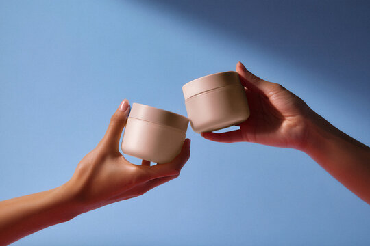 Mockup di barattoli di crema beige tenuti da mani femminili su sfondo blu