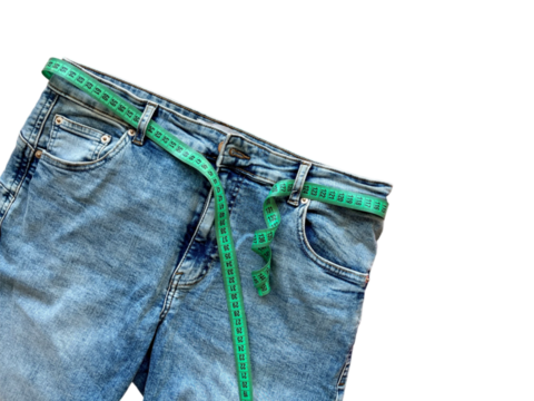 Jeans and green measuring tape instead of a belt on a transparent background. Concept of weight loss, diet, detox, thin waist. Copy space for text