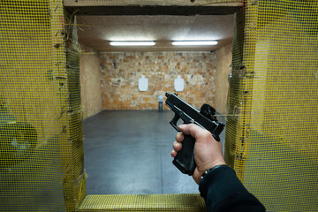 First person view: shooter aims a pistol at targets in a safe indoor shooting range, practicing...