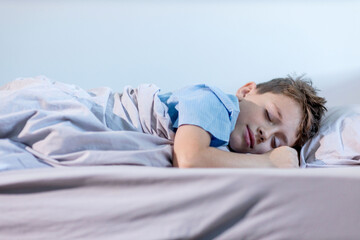 A young boy wearing a blue shirt is peacefully sleeping on his cozy bed tucked in with soft...