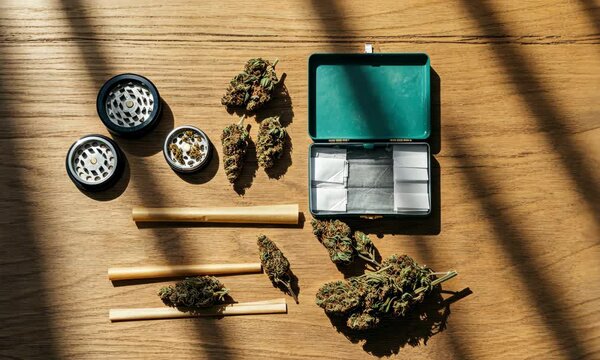 Cannabis buds, grinder, and rolling papers on wooden surface