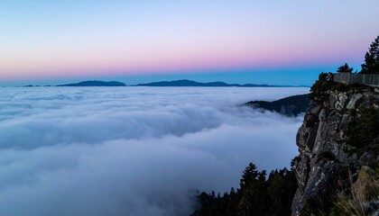 Fototapeta premium Wide shot from the edge of a mountain cliff at twilight with low clouds rolling in below