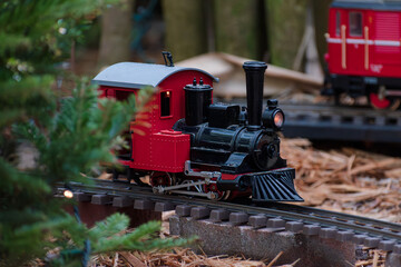 Miniature electric toy train circling a track around a Christmas tree on a bed a mulch with other...