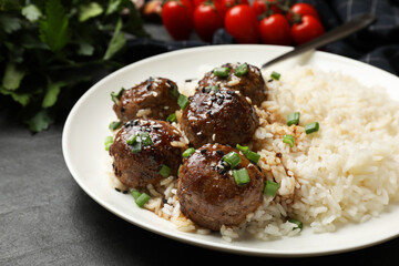 Delicious rice with meatballs, sauce and green onions on black table, closeup