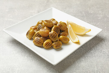 Grilled green olives and lemon wedges on gray textured table, closeup