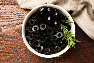 Delicious marinated olive rings and rosemary in bowl on wooden table, top view