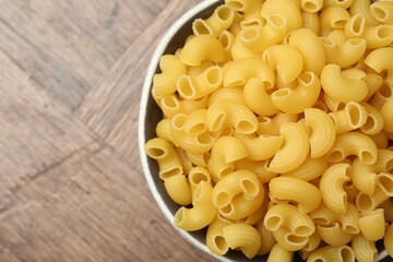 Raw horns pasta in bowl on wooden table, top view. Space for text
