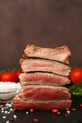 Delicious sliced beef tenderloin with different degrees of doneness and spices on table against brown background, closeup