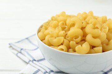 Raw horns pasta in bowl on white table, closeup