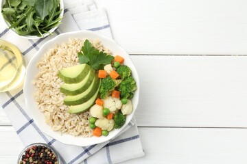 Tasty brown rice with vegetables and products on white wooden table, flat lay. Space for text