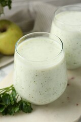 Healthy parsley drink in glasses and leaves on table, closeup