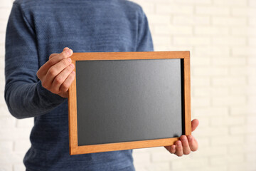 Man holding blank small blackboard indoors, closeup